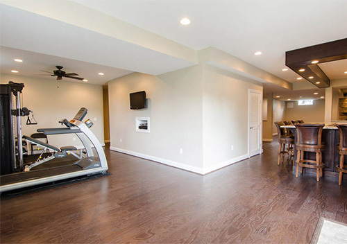 Remodeled basement with wood flooring, exercise area and sitting area with wood chairs, done for Alexandria basement renovation.