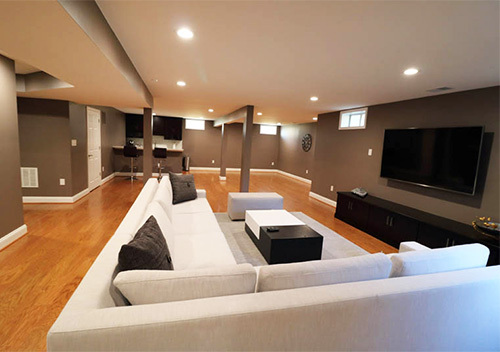 Large white couch surrounding a wall-mounted TV, an example of our basement remodel services near Alexandria, VA.